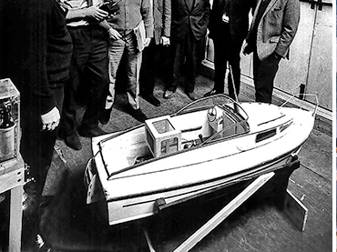 John Stears shows off a radio-controlled model of a Fairey Huntress motor boat to colleagues at Pinewood Studios
